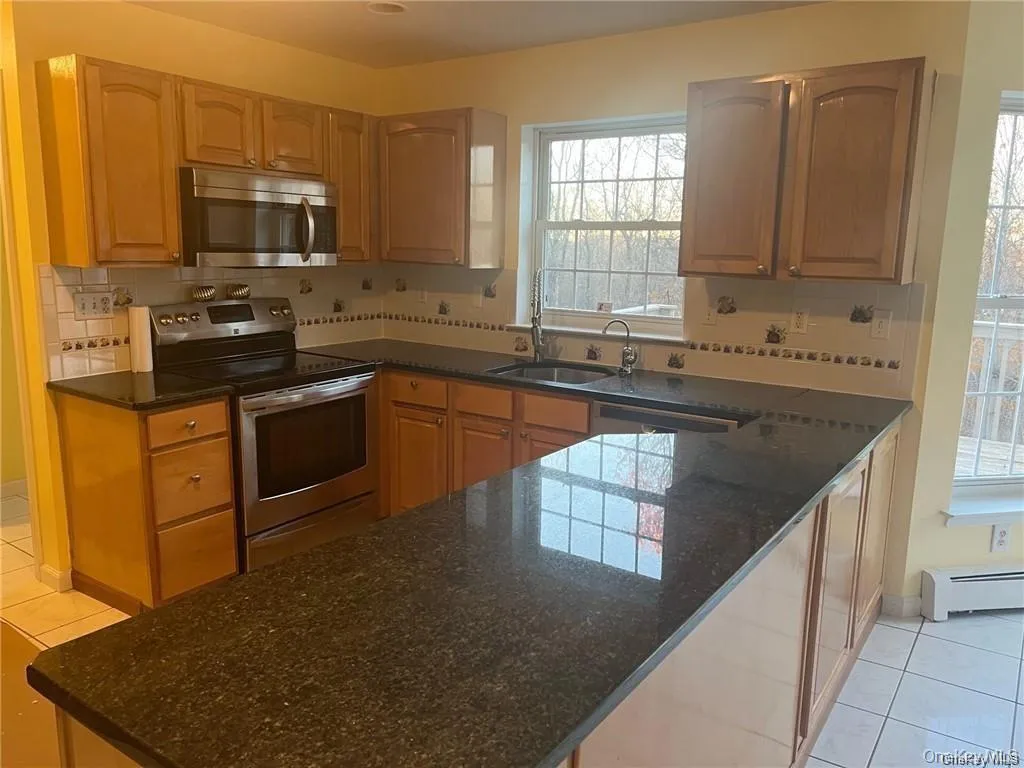 Kitchen featuring light tile patterned flooring, stainless steel appliances, dark stone counters, and tasteful backsplash Kitchen featuring light tile patterned flooring, stainless steel appliances, dark stone counters, and tasteful backsplash