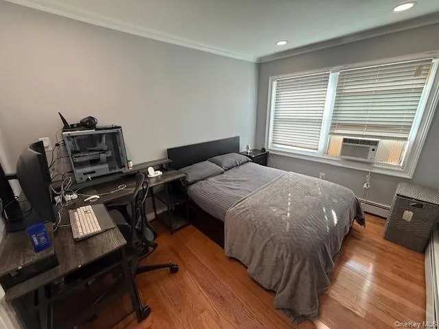 Bedroom featuring ornamental molding, a desk, wood finished floors, a baseboard radiator, and cooling unit Bedroom featuring ornamental molding, a desk, wood finished floors, a baseboard radiator, and cooling unit