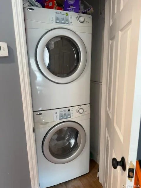 Laundry area featuring stacked washing machine and dryer and wood finished floors Laundry area featuring stacked washing machine and dryer and wood finished floors