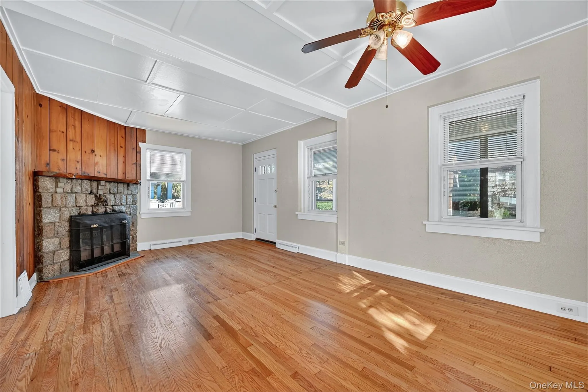 Living room featuring a stone fireplace, light wood-type flooring, coffered ceiling, and a ceiling fan Living room featuring a stone fireplace, light wood-type flooring, coffered ceiling, and a ceiling fan