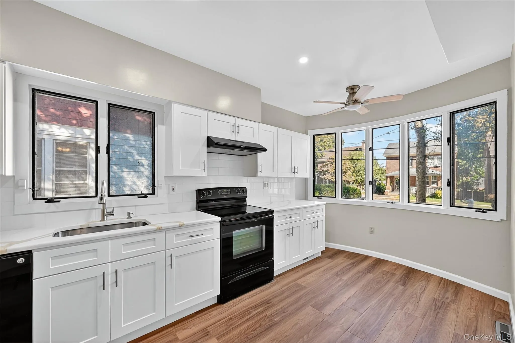 Kitchen with black / electric stove, white cabinetry, decorative backsplash, light wood-style floors, and under cabinet range hood Kitchen with black / electric stove, white cabinetry, decorative backsplash, light wood-style floors, and under cabinet range hood