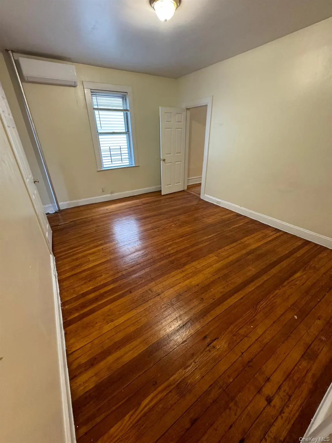 Unfurnished bedroom with hardwood / wood-style floors and an AC wall unit Unfurnished bedroom with hardwood / wood-style floors and an AC wall unit
