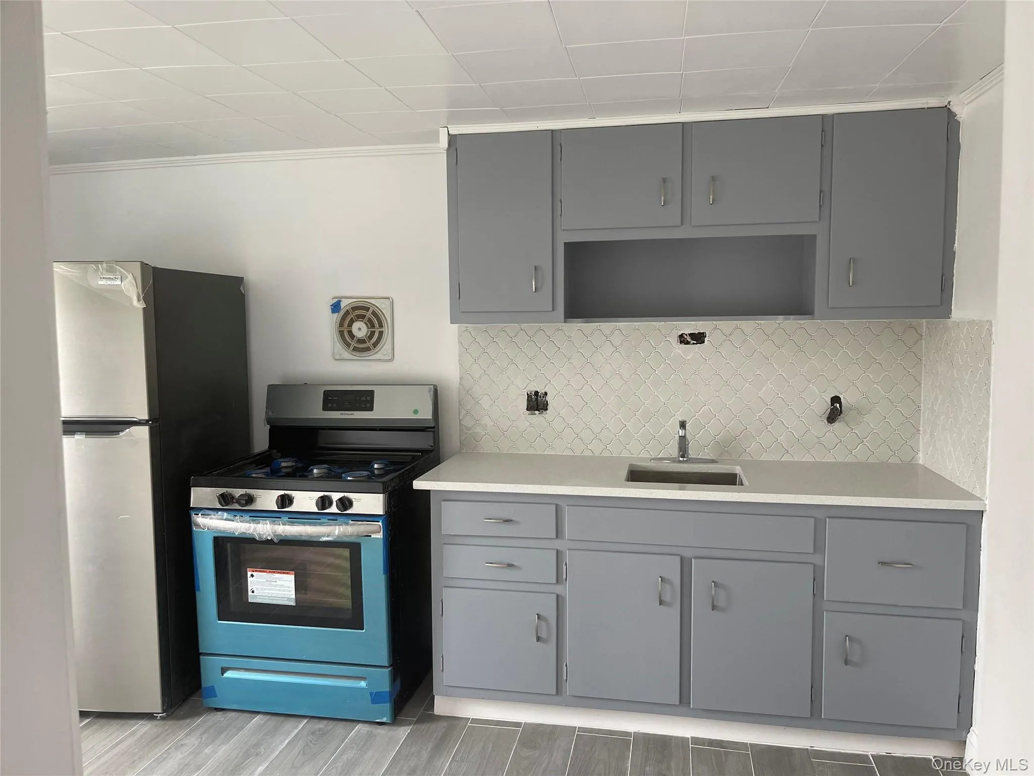 Kitchen with gray cabinetry, appliances with stainless steel finishes, tasteful backsplash, wood tiled floors, and open shelves Kitchen with gray cabinetry, appliances with stainless steel finishes, tasteful backsplash, wood tiled floors, and open shelves