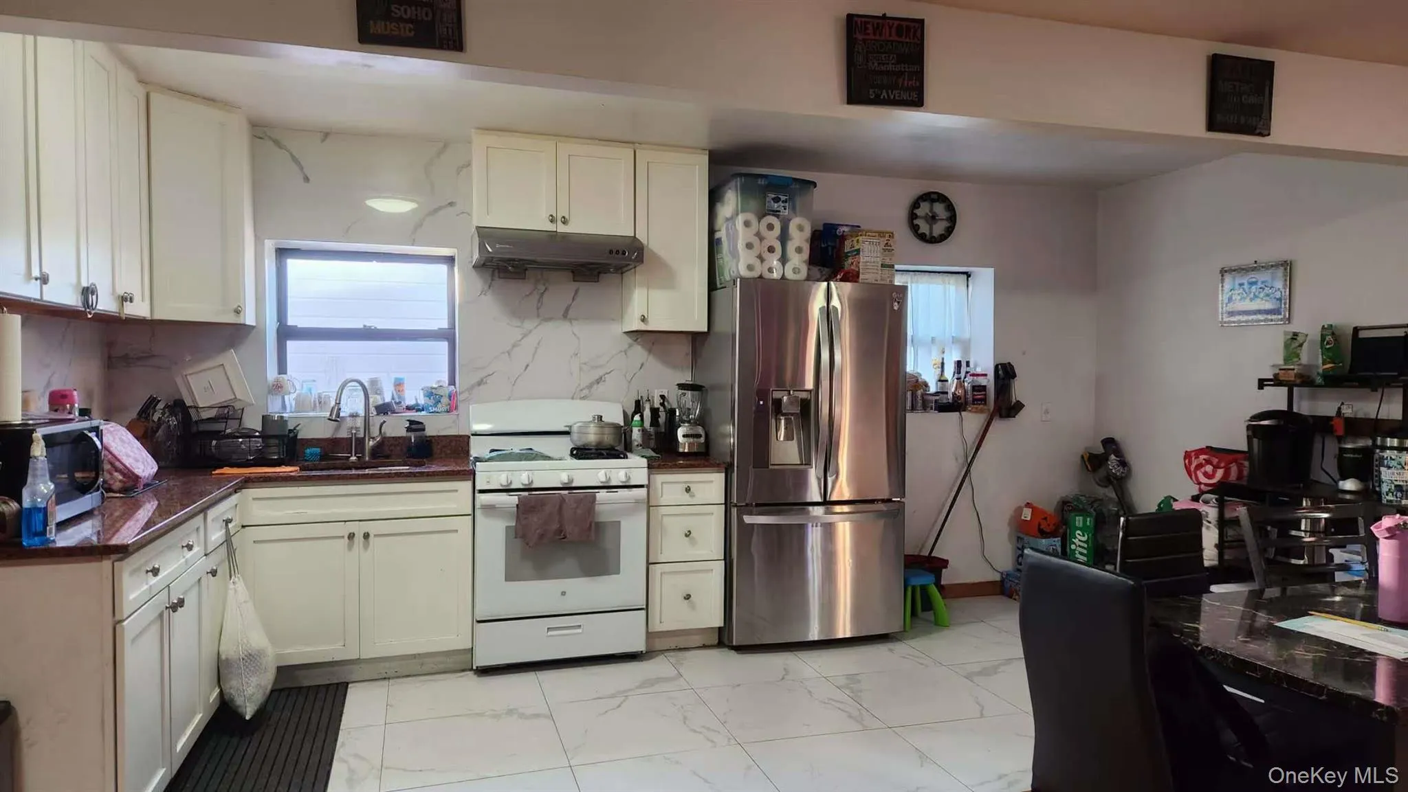 Kitchen featuring white gas range oven, stainless steel fridge with ice dispenser, light marble finish flooring, under cabinet range hood, and backsplash Kitchen featuring white gas range oven, stainless steel fridge with ice dispenser, light marble finish flooring, under cabinet range hood, and backsplash
