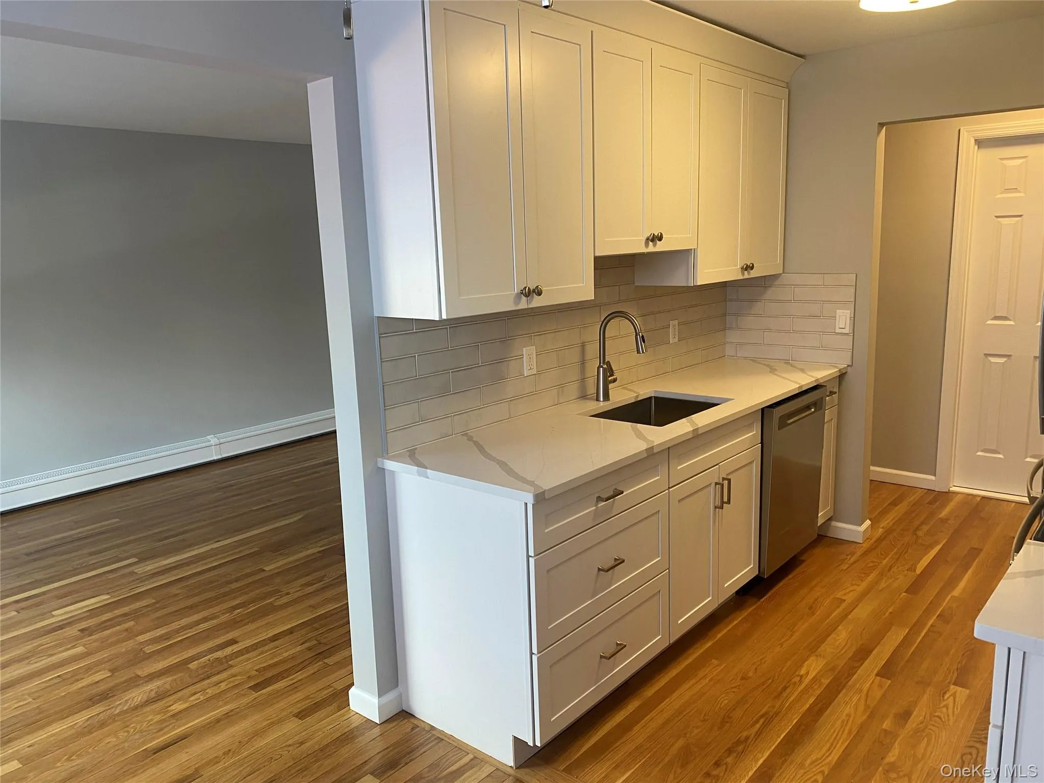 Kitchen with white cabinets, tasteful backsplash, dishwasher, light stone counters, and light wood-type flooring Kitchen with white cabinets, tasteful backsplash, dishwasher, light stone counters, and light wood-type flooring