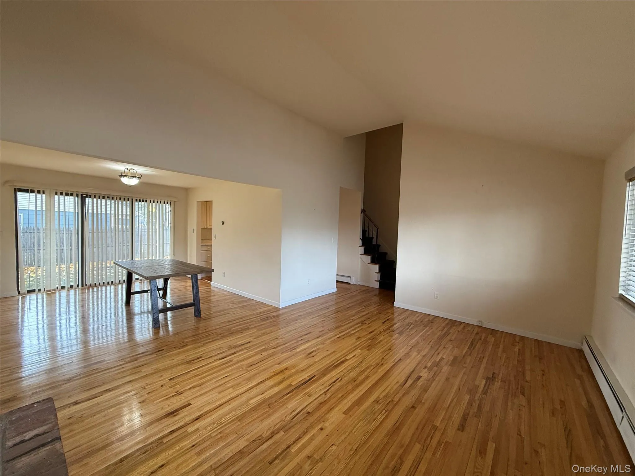 Unfurnished living room featuring baseboard heating, lofted ceiling, stairs, and light wood finished floors Unfurnished living room featuring baseboard heating, lofted ceiling, stairs, and light wood finished floors
