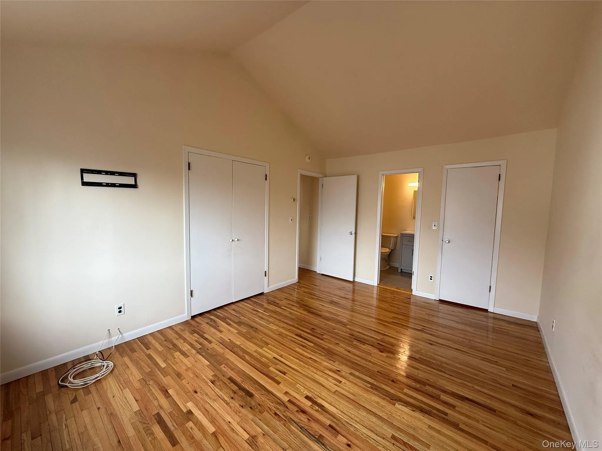 Unfurnished bedroom with hardwood / wood-style flooring, ensuite bathroom, and high vaulted ceiling Unfurnished bedroom with hardwood / wood-style flooring, ensuite bathroom, and high vaulted ceiling