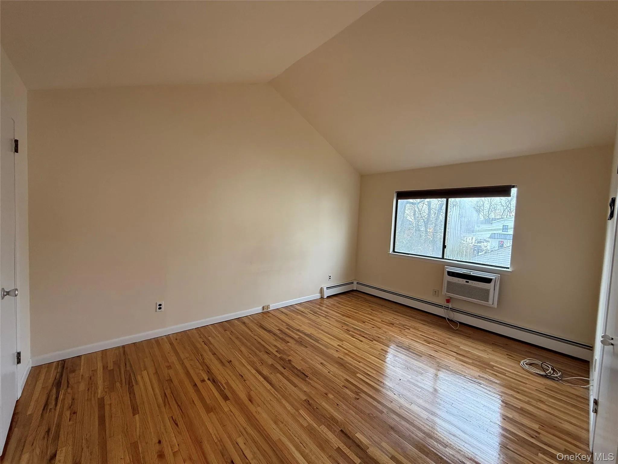 Spare room with light wood-style flooring, a baseboard radiator, lofted ceiling, and a wall mounted AC Spare room with light wood-style flooring, a baseboard radiator, lofted ceiling, and a wall mounted AC