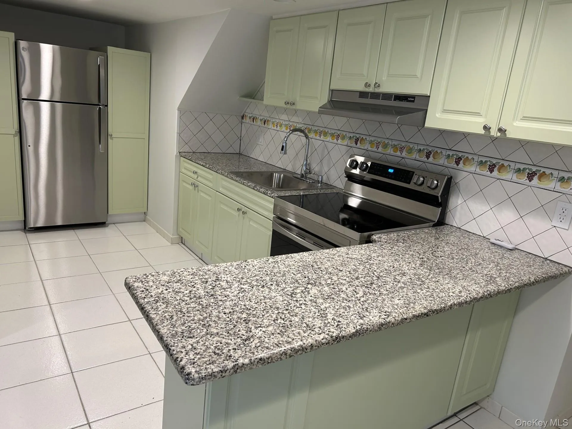 Kitchen with light stone countertops, stainless steel appliances, light tile patterned flooring, backsplash, and under cabinet range hood Kitchen with light stone countertops, stainless steel appliances, light tile patterned flooring, backsplash, and under cabinet range hood