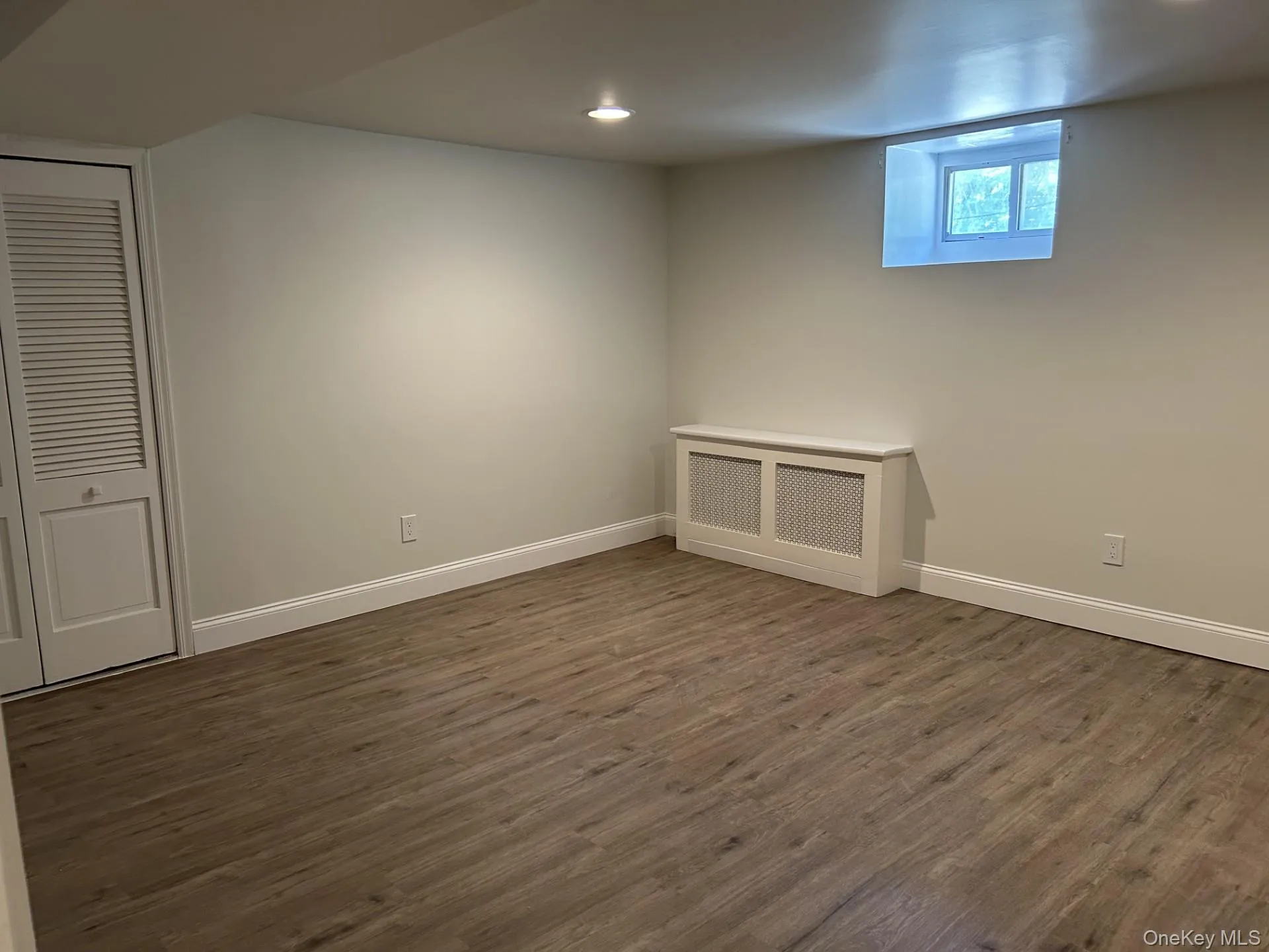 Below grade area with radiator heating unit, dark wood-style floors, and recessed lighting Below grade area with radiator heating unit, dark wood-style floors, and recessed lighting