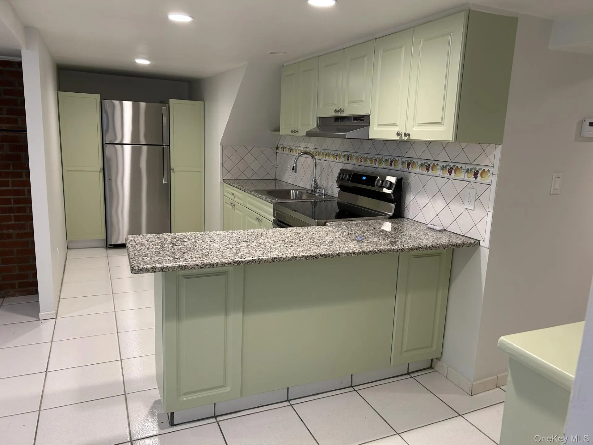 Kitchen featuring green cabinetry, appliances with stainless steel finishes, light stone counters, backsplash, and under cabinet range hood Kitchen featuring green cabinetry, appliances with stainless steel finishes, light stone counters, backsplash, and under cabinet range hood