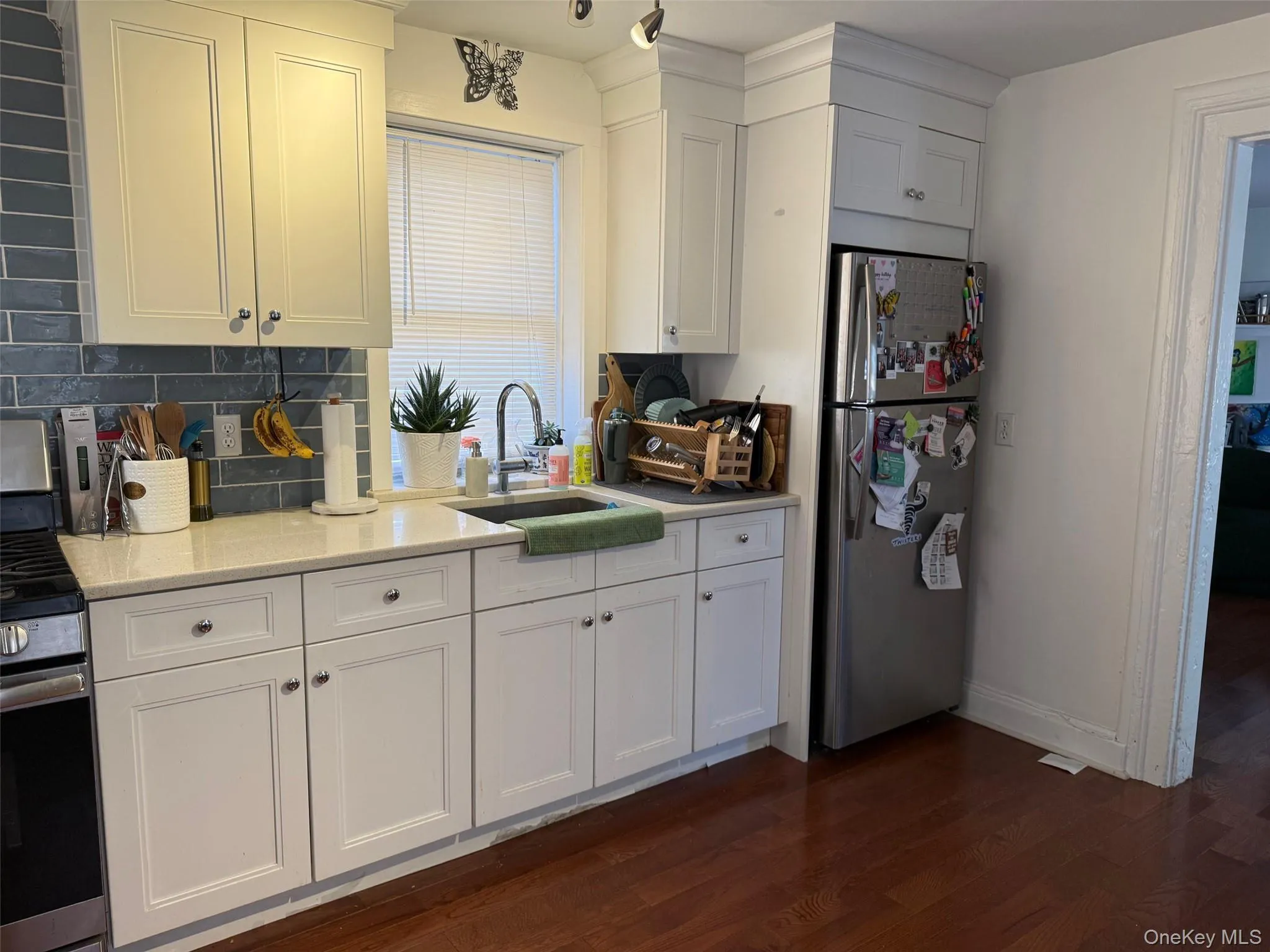 Kitchen featuring appliances with stainless steel finishes, white cabinetry, dark wood-type flooring, light stone counters, and decorative backsplash Kitchen featuring appliances with stainless steel finishes, white cabinetry, dark wood-type flooring, light stone counters, and decorative backsplash