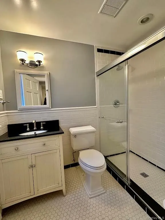 Bathroom featuring a shower stall, vanity, wainscoting, and tile walls Bathroom featuring a shower stall, vanity, wainscoting, and tile walls