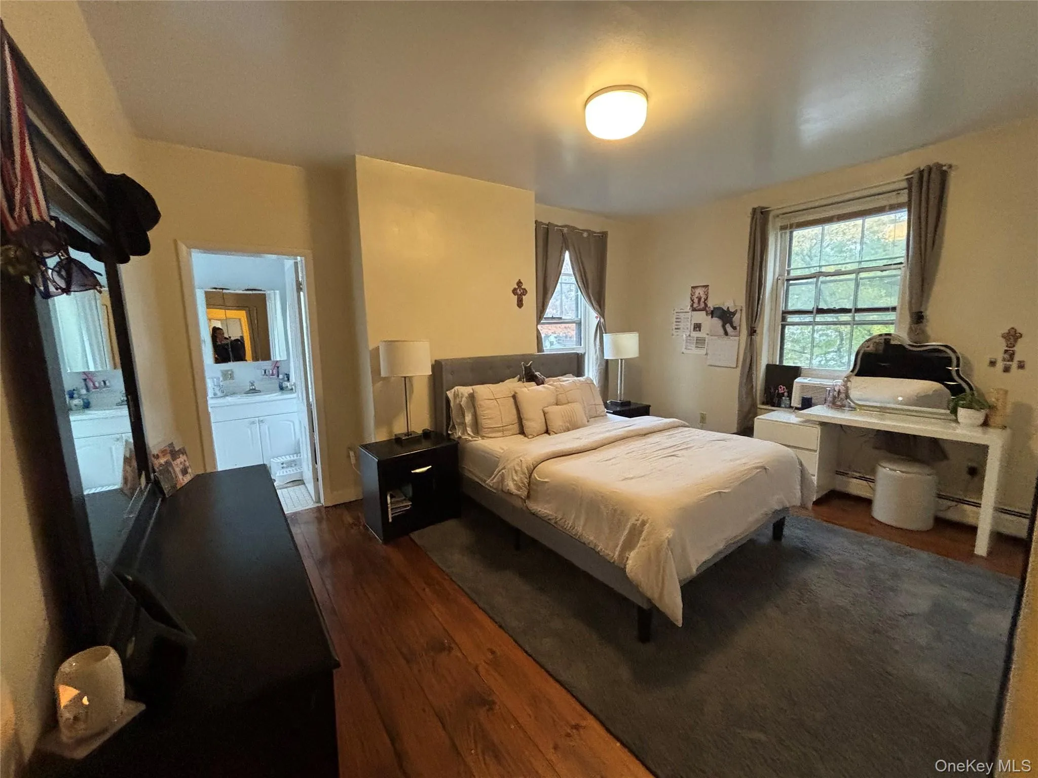 Bedroom featuring dark wood finished floors, baseboard heating, and connected bathroom Bedroom featuring dark wood finished floors, baseboard heating, and connected bathroom