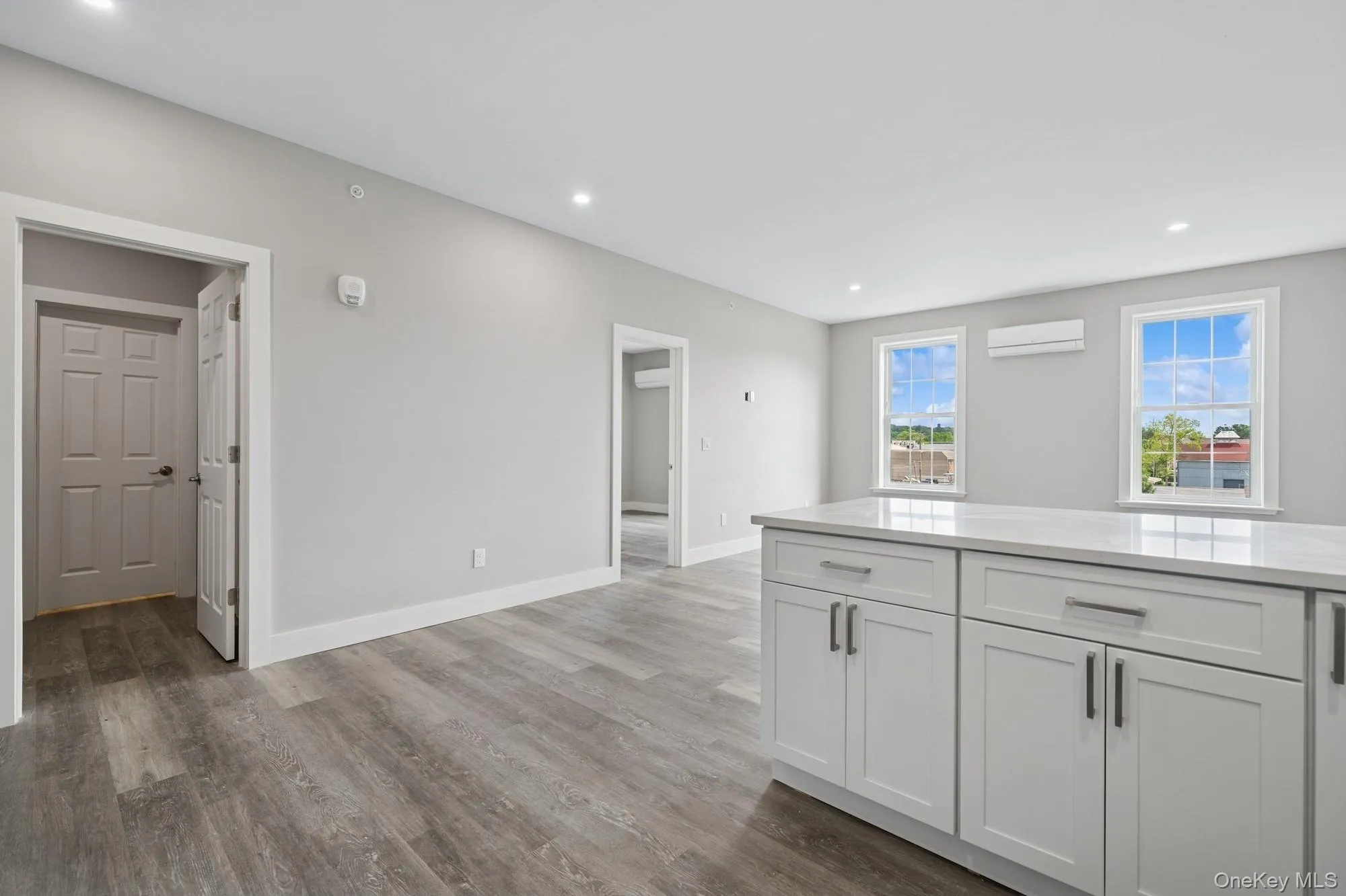 Kitchen with light stone counters, white cabinets, recessed lighting, dark wood-style floors, and an AC wall unit Kitchen with light stone counters, white cabinets, recessed lighting, dark wood-style floors, and an AC wall unit