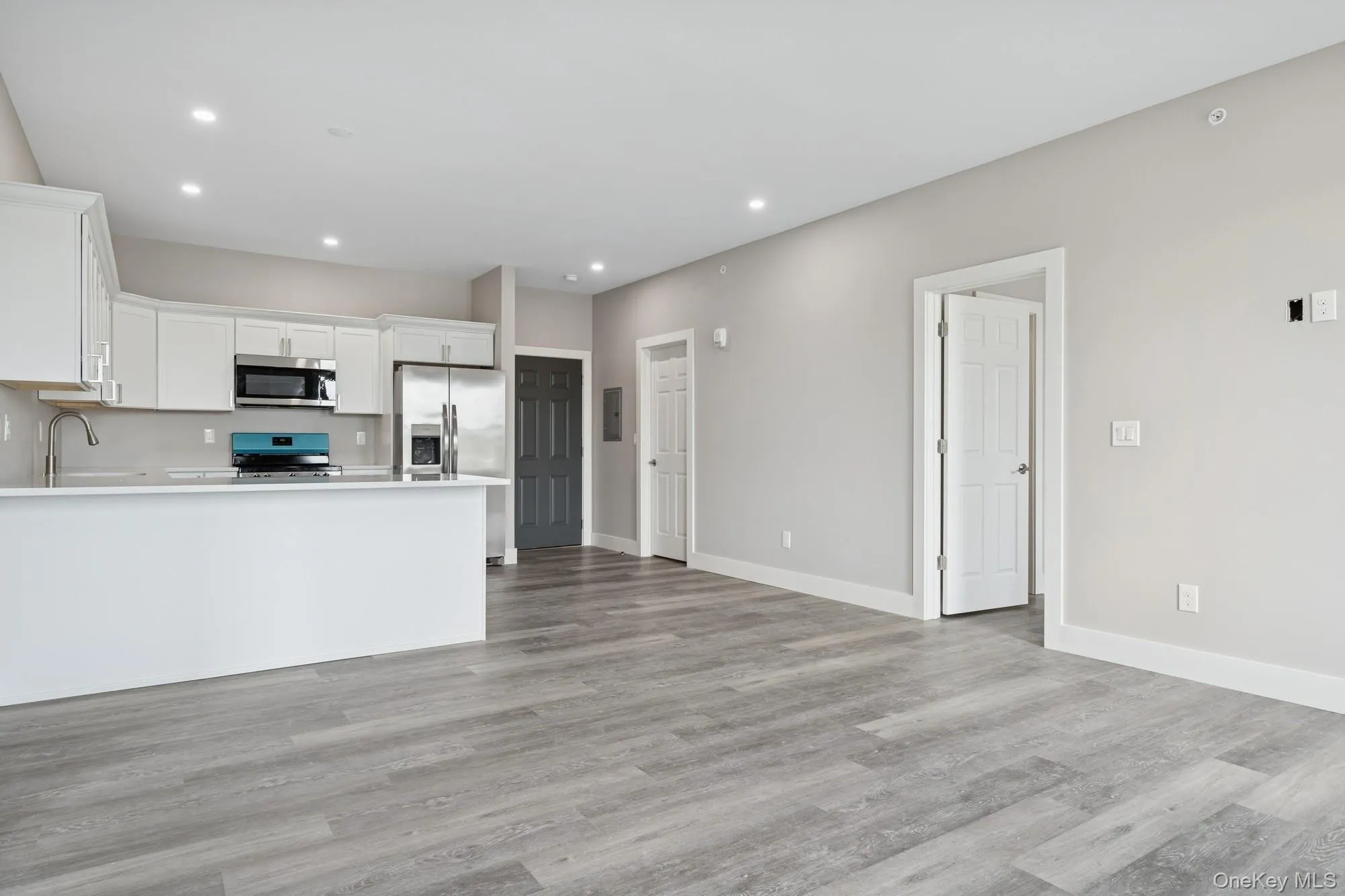 Kitchen with white cabinetry, stainless steel appliances, open floor plan, recessed lighting, and light wood finished floors Kitchen with white cabinetry, stainless steel appliances, open floor plan, recessed lighting, and light wood finished floors