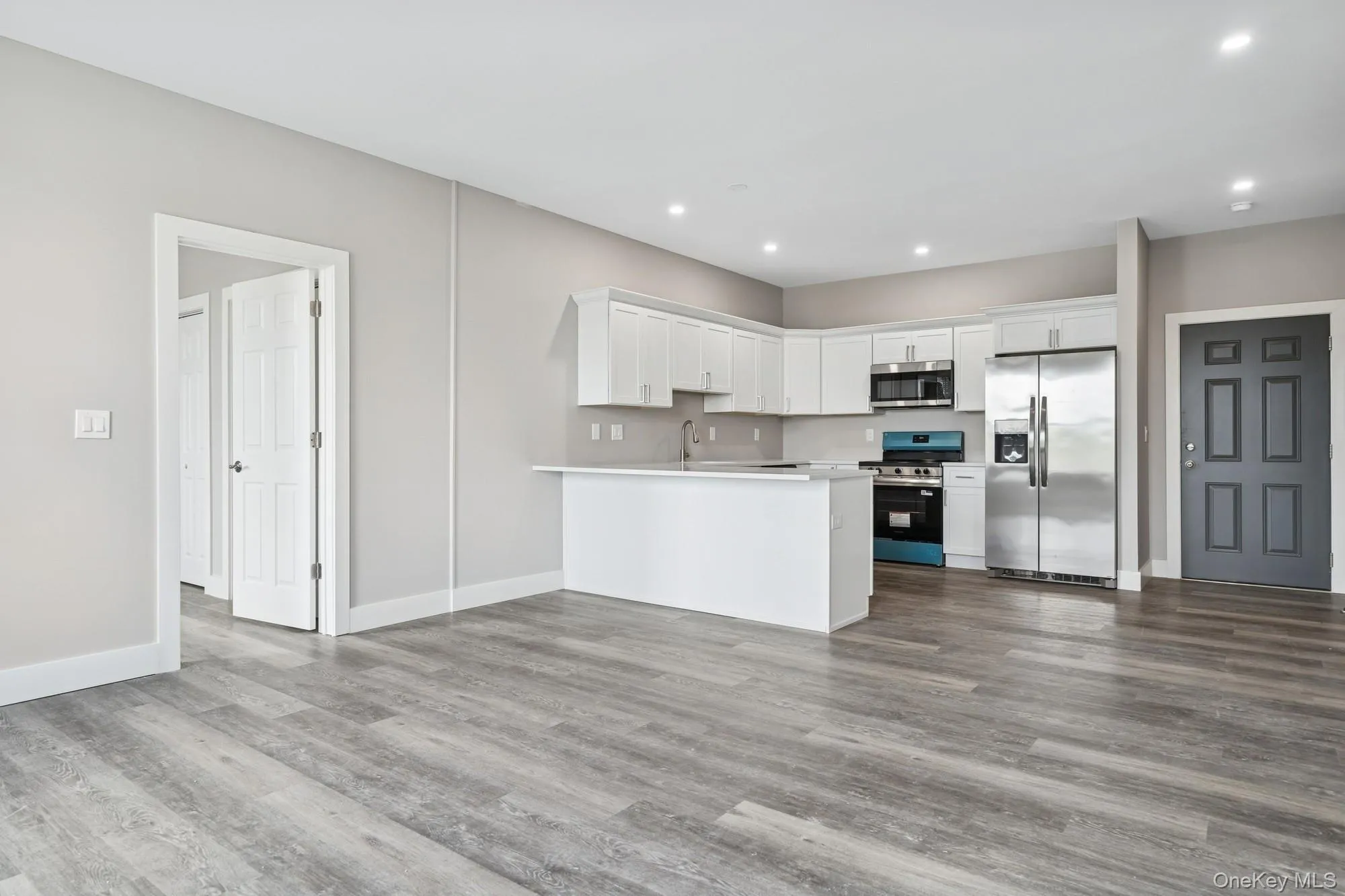 Kitchen with stainless steel appliances, light countertops, white cabinets, a peninsula, and dark wood-style flooring Kitchen with stainless steel appliances, light countertops, white cabinets, a peninsula, and dark wood-style flooring