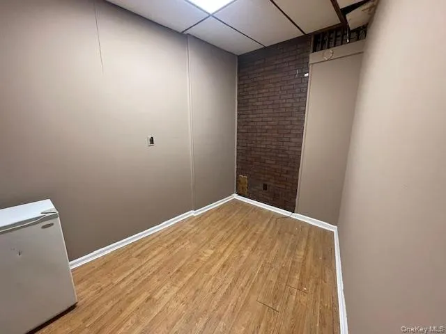 Spare room with brick wall, light wood-style flooring, and a paneled ceiling Spare room with brick wall, light wood-style flooring, and a paneled ceiling