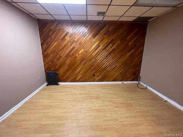Spare room with an accent wall, wood walls, light wood finished floors, radiator heating unit, and a paneled ceiling Spare room with an accent wall, wood walls, light wood finished floors, radiator heating unit, and a paneled ceiling