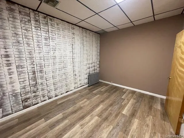 Empty room with a paneled ceiling, radiator heating unit, and wood finished floors Empty room with a paneled ceiling, radiator heating unit, and wood finished floors