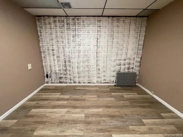 Unfurnished room with a drop ceiling, radiator, and light wood-style floors Unfurnished room with a drop ceiling, radiator, and light wood-style floors