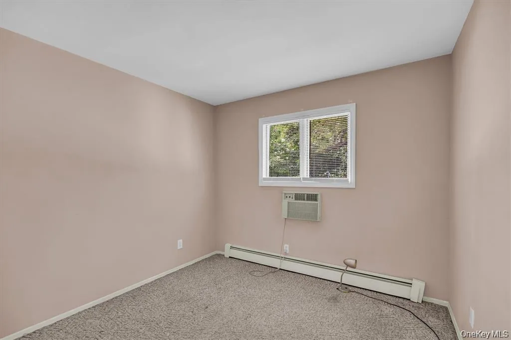 Empty room with a baseboard heating unit, carpet floors, and an AC wall unit Empty room with a baseboard heating unit, carpet floors, and an AC wall unit