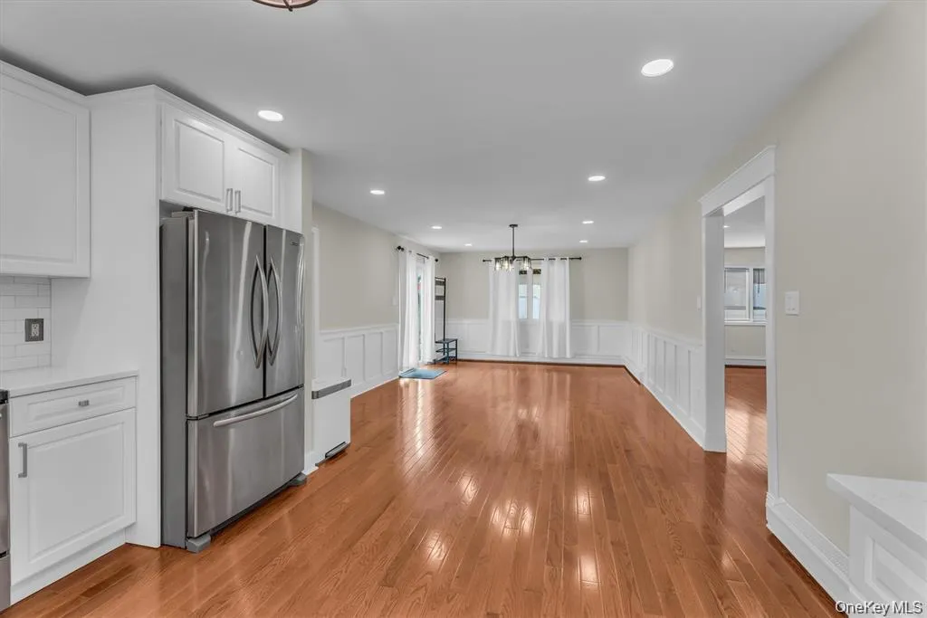 Kitchen featuring freestanding refrigerator, white cabinets, a decorative wall, a wainscoted wall, and light stone counters Kitchen featuring freestanding refrigerator, white cabinets, a decorative wall, a wainscoted wall, and light stone counters