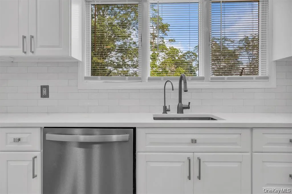 Kitchen with white cabinetry, stainless steel dishwasher, light stone counters, and backsplash Kitchen with white cabinetry, stainless steel dishwasher, light stone counters, and backsplash