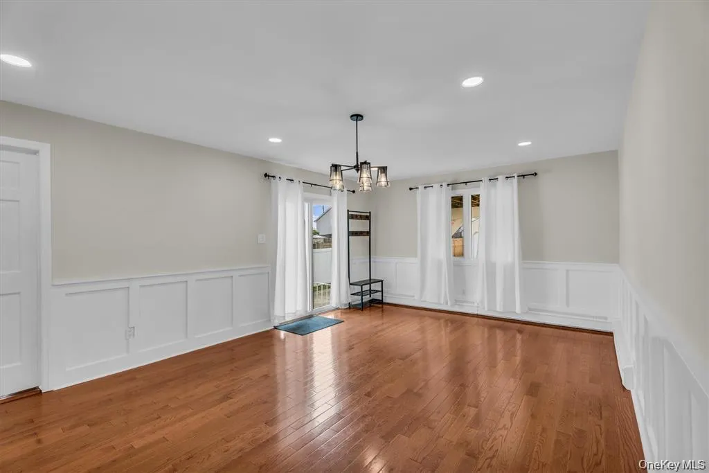 Empty room featuring a chandelier, wood-type flooring, a wainscoted wall, and recessed lighting Empty room featuring a chandelier, wood-type flooring, a wainscoted wall, and recessed lighting