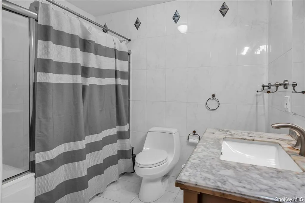 Full bathroom featuring vanity, tile walls, and light tile patterned floors Full bathroom featuring vanity, tile walls, and light tile patterned floors
