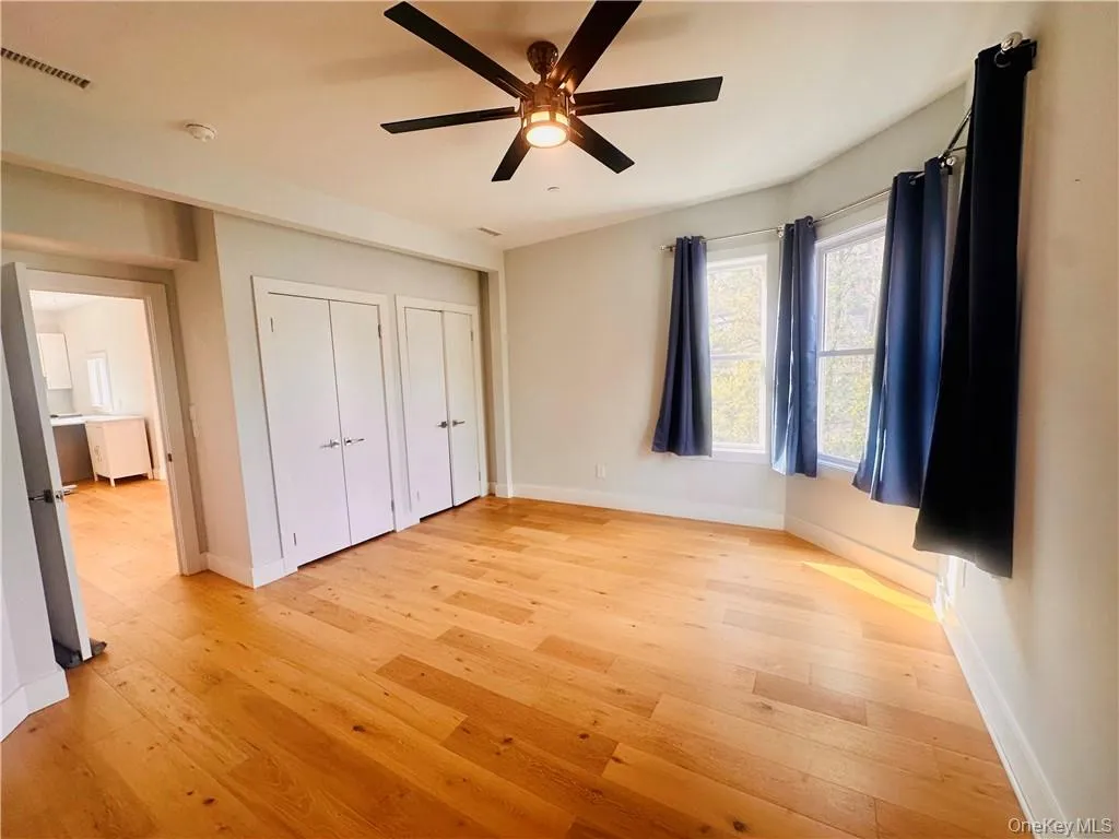 Unfurnished bedroom with ceiling fan, light wood-type flooring, and two closets Unfurnished bedroom with ceiling fan, light wood-type flooring, and two closets