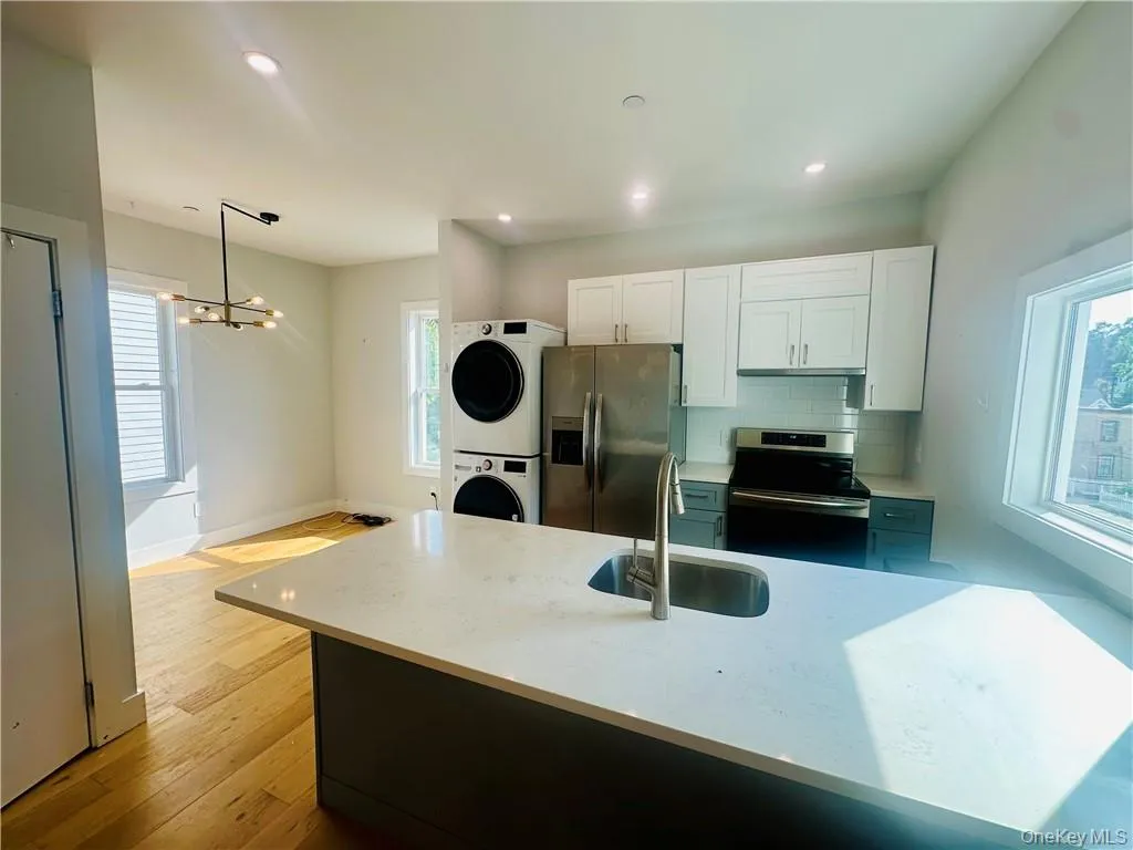 Kitchen with hanging light fixtures, sink, stacked washing maching and dryer, appliances with stainless steel finishes, and a notable chandelier Kitchen with hanging light fixtures, sink, stacked washing maching and dryer, appliances with stainless steel finishes, and a notable chandelier