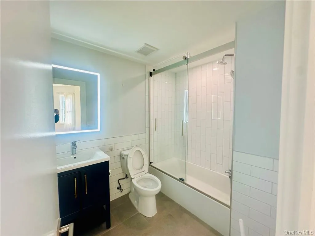 Full bathroom featuring tile walls, vanity, enclosed tub / shower combo, tile patterned flooring, and toilet Full bathroom featuring tile walls, vanity, enclosed tub / shower combo, tile patterned flooring, and toilet