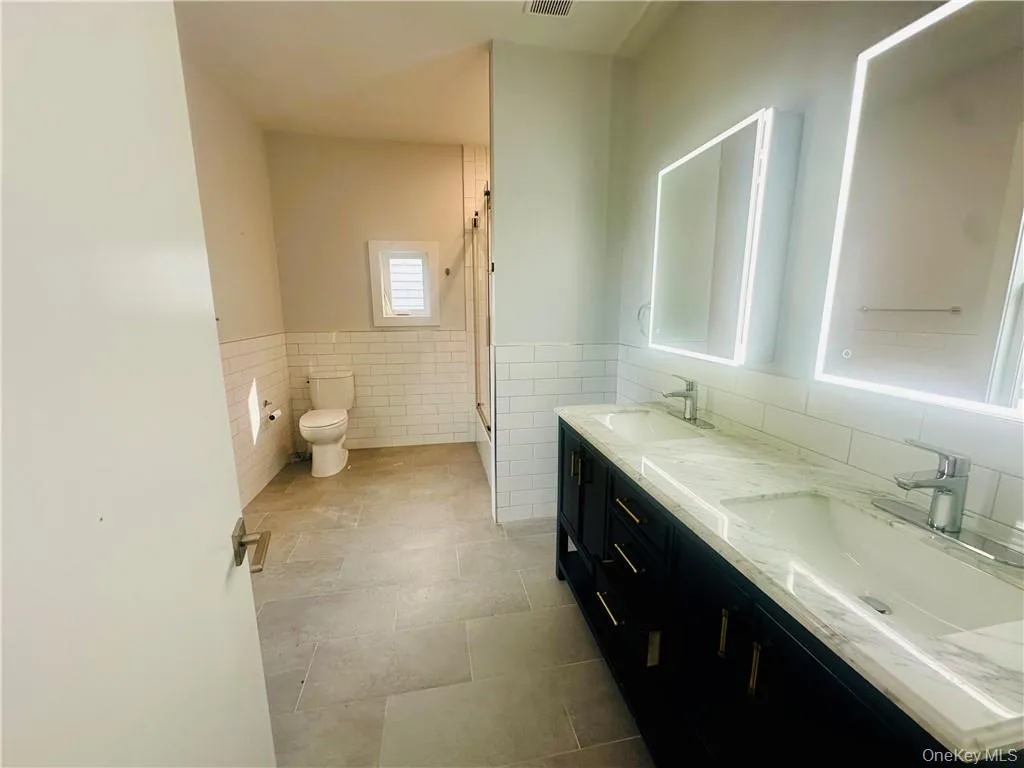 Bathroom featuring tile walls, tile patterned floors, vanity, and toilet Bathroom featuring tile walls, tile patterned floors, vanity, and toilet