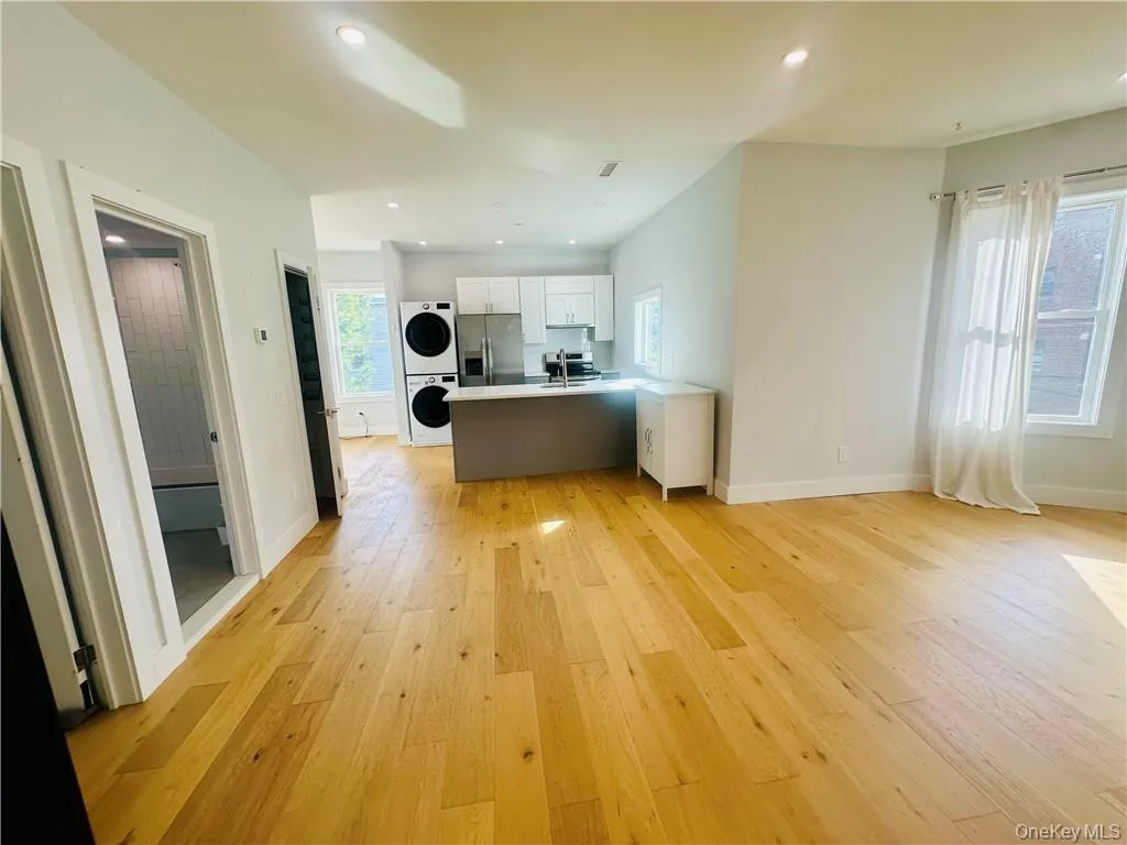 Kitchen with stacked washer / drying machine, stainless steel fridge, light hardwood / wood-style floors, and white cabinets Kitchen with stacked washer / drying machine, stainless steel fridge, light hardwood / wood-style floors, and white cabinets