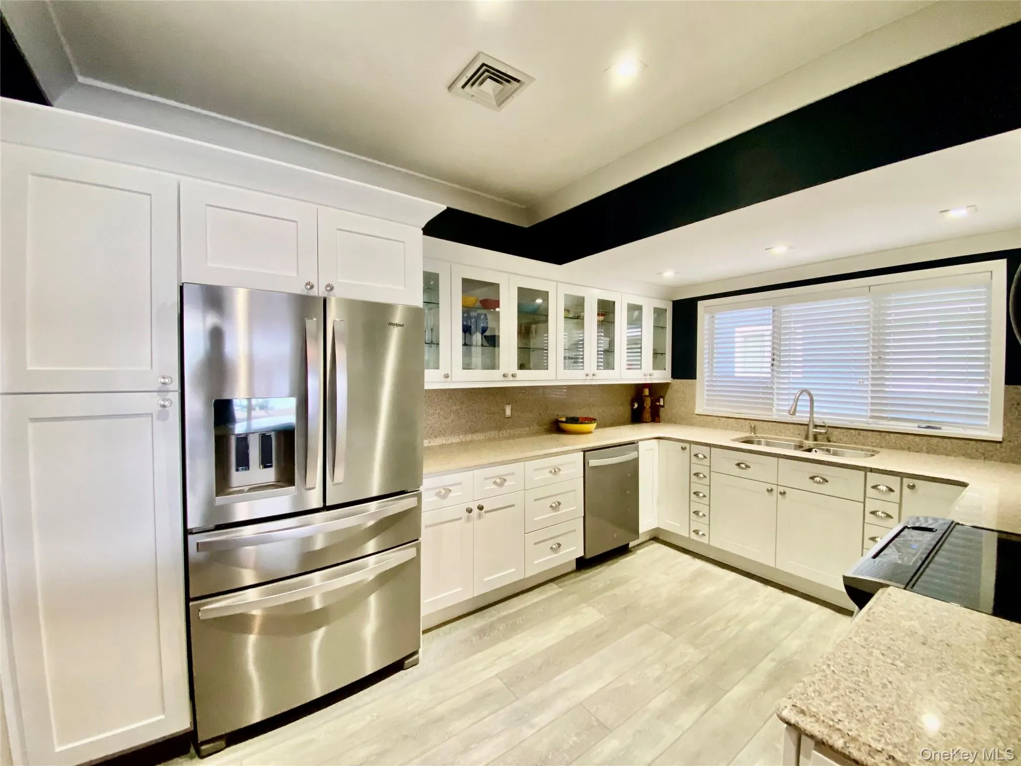 Kitchen featuring stainless steel appliances, white cabinetry, glass insert cabinets, light stone countertops, and light wood-style floors Kitchen featuring stainless steel appliances, white cabinetry, glass insert cabinets, light stone countertops, and light wood-style floors