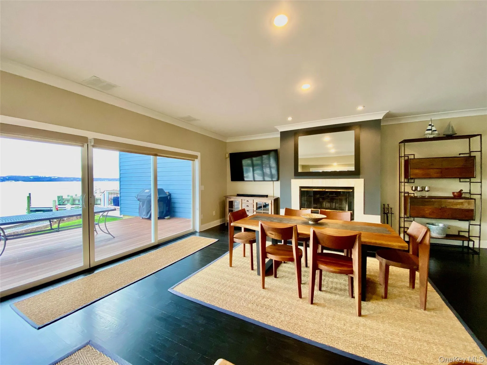 Dining space featuring recessed lighting, wood finished floors, ornamental molding, a glass covered fireplace, and a water view Dining space featuring recessed lighting, wood finished floors, ornamental molding, a glass covered fireplace, and a water view