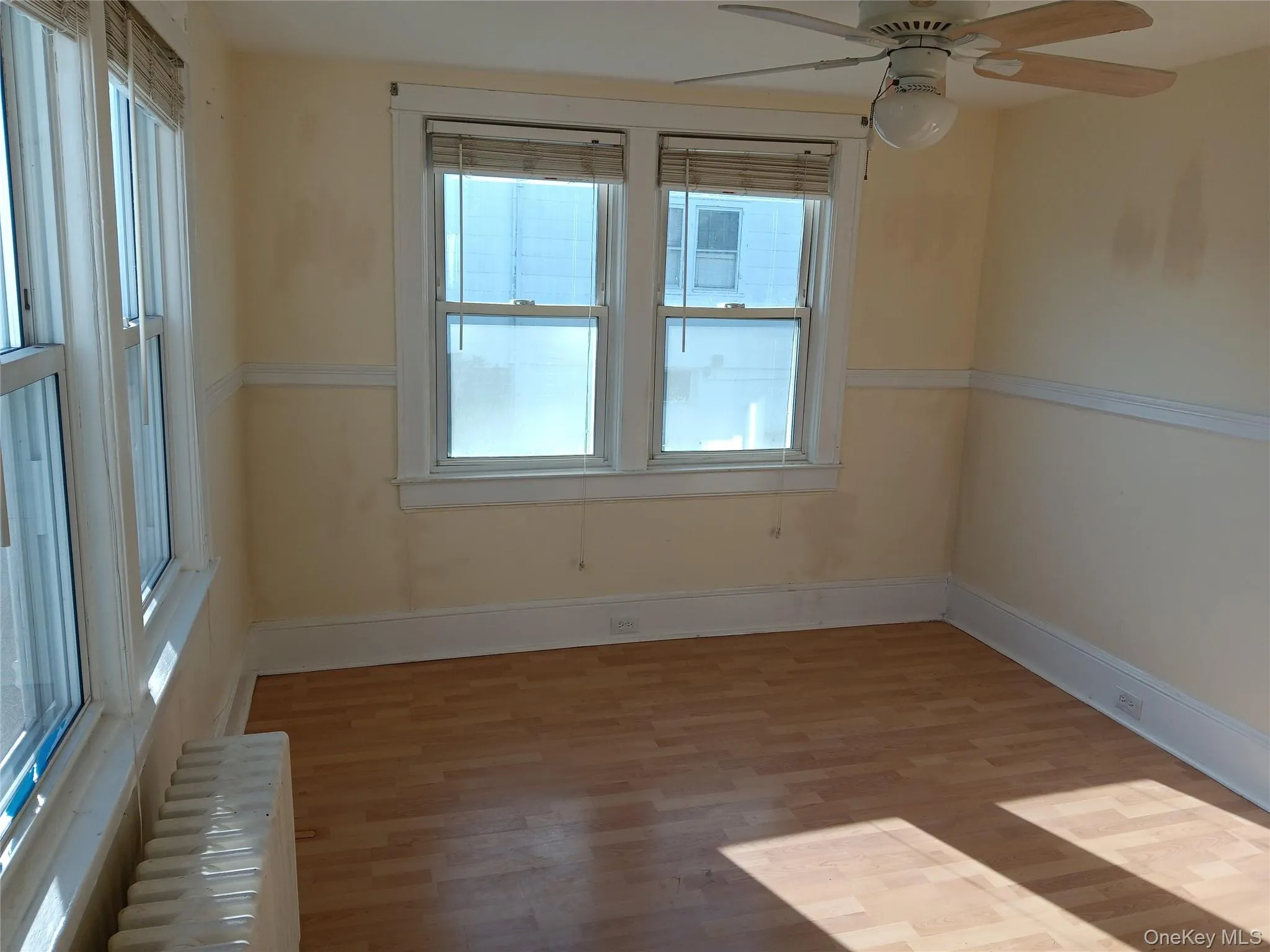 Spare room with radiator heating unit, light wood-style floors, and ceiling fan Spare room with radiator heating unit, light wood-style floors, and ceiling fan