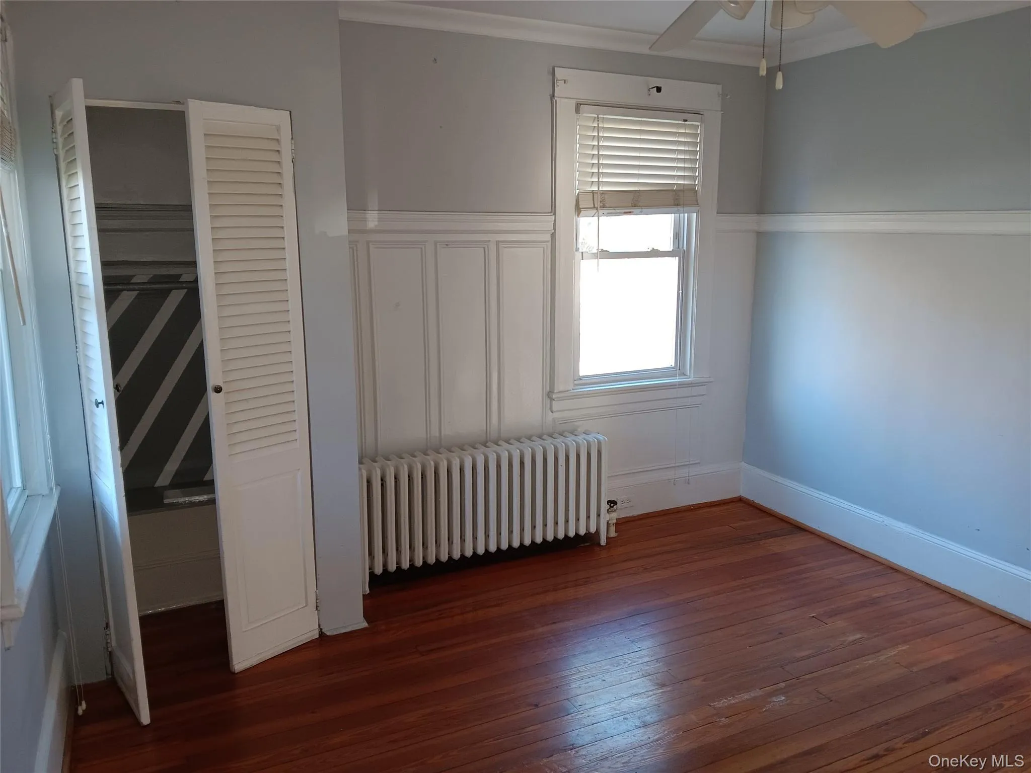 Unfurnished bedroom featuring radiator, dark wood finished floors, ceiling fan, and ornamental molding Unfurnished bedroom featuring radiator, dark wood finished floors, ceiling fan, and ornamental molding