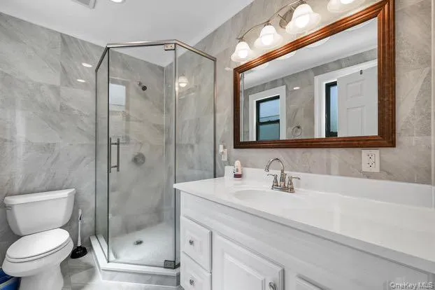 Bathroom featuring tile walls, vanity, a stall shower, and light marble finish flooring Bathroom featuring tile walls, vanity, a stall shower, and light marble finish flooring