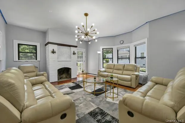 Living room featuring healthy amount of natural light, a brick fireplace, a chandelier, and radiator Living room featuring healthy amount of natural light, a brick fireplace, a chandelier, and radiator