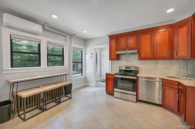 Kitchen with appliances with stainless steel finishes, backsplash, a wall mounted air conditioner, recessed lighting, and under cabinet range hood Kitchen with appliances with stainless steel finishes, backsplash, a wall mounted air conditioner, recessed lighting, and under cabinet range hood