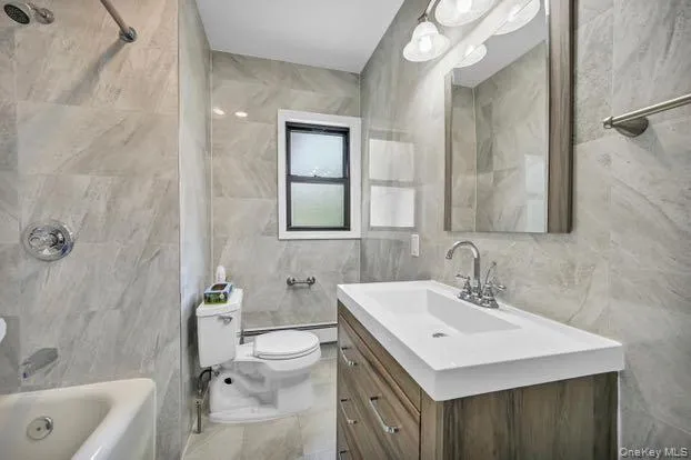 Bathroom featuring vanity, tile walls, tub / shower combination, and baseboard heating Bathroom featuring vanity, tile walls, tub / shower combination, and baseboard heating