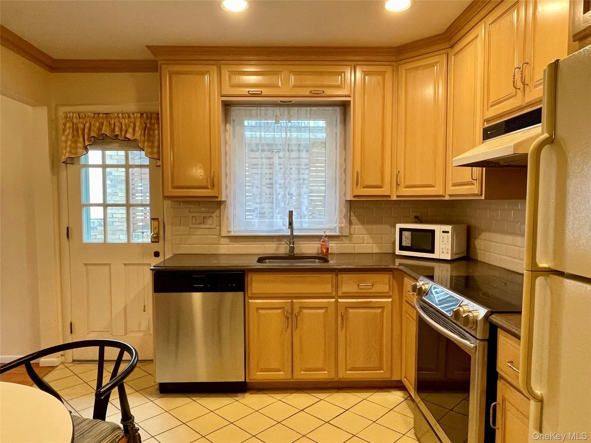 Kitchen with stainless steel appliances, tasteful backsplash, under cabinet range hood, light tile patterned flooring, and ornamental molding Kitchen with stainless steel appliances, tasteful backsplash, under cabinet range hood, light tile patterned flooring, and ornamental molding