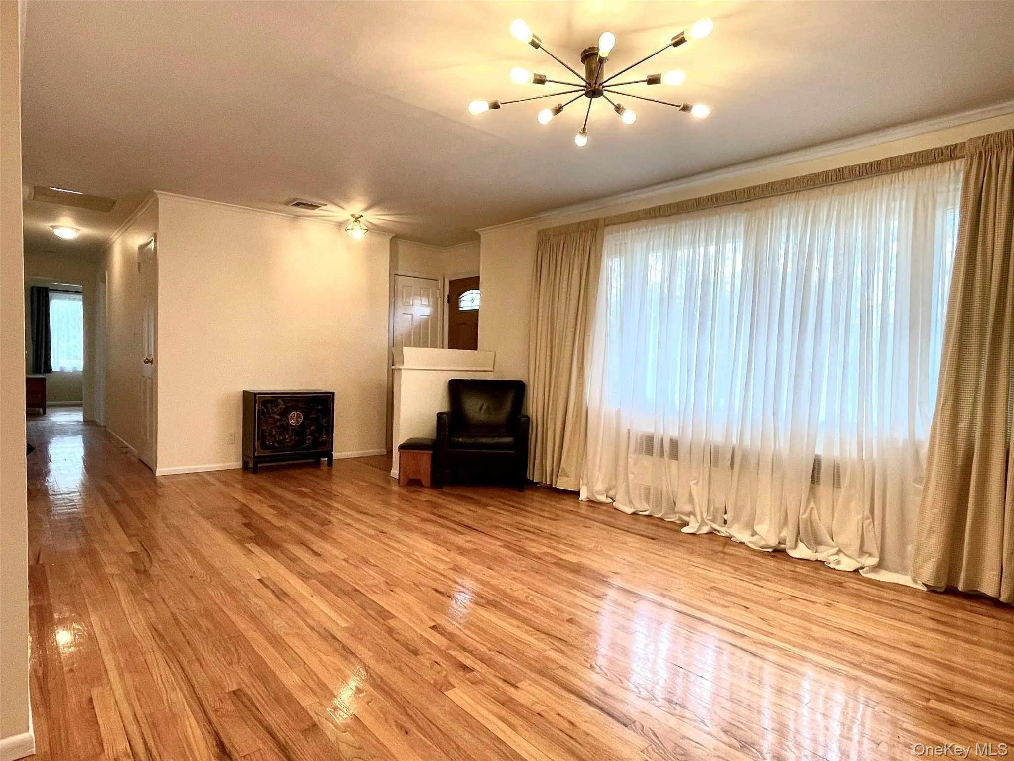 Unfurnished living room featuring ornamental molding, wood finished floors, and a chandelier Unfurnished living room featuring ornamental molding, wood finished floors, and a chandelier