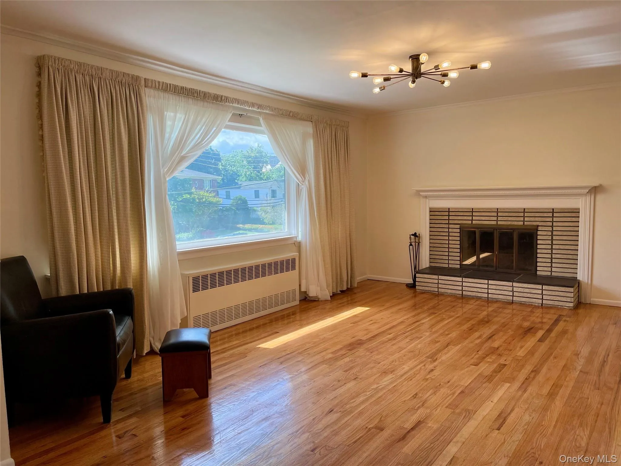 Unfurnished living room with radiator heating unit, a fireplace, light wood-type flooring, a chandelier, and crown molding Unfurnished living room with radiator heating unit, a fireplace, light wood-type flooring, a chandelier, and crown molding