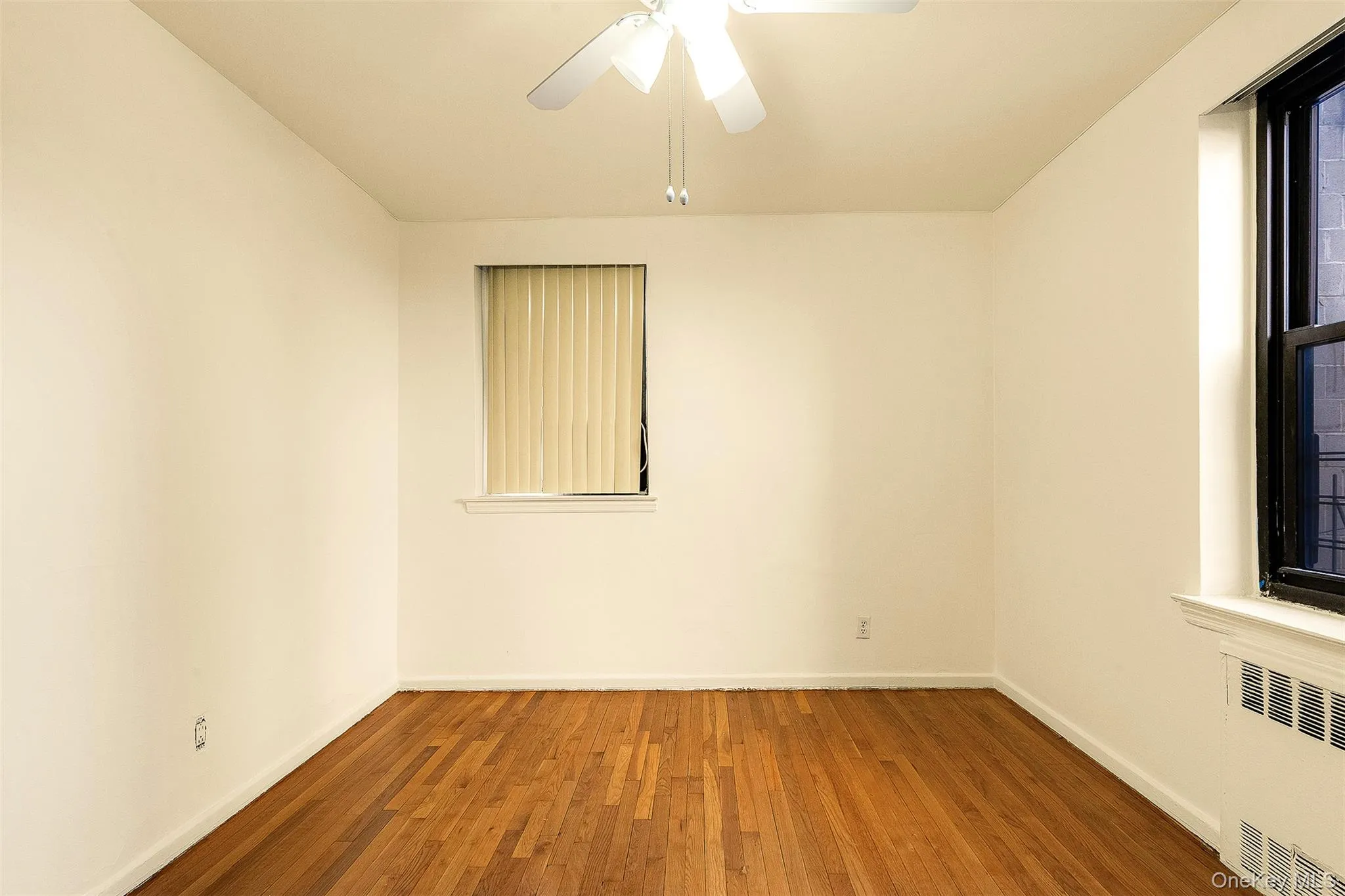 Unfurnished room featuring hardwood / wood-style floors, radiator, and a ceiling fan Unfurnished room featuring hardwood / wood-style floors, radiator, and a ceiling fan