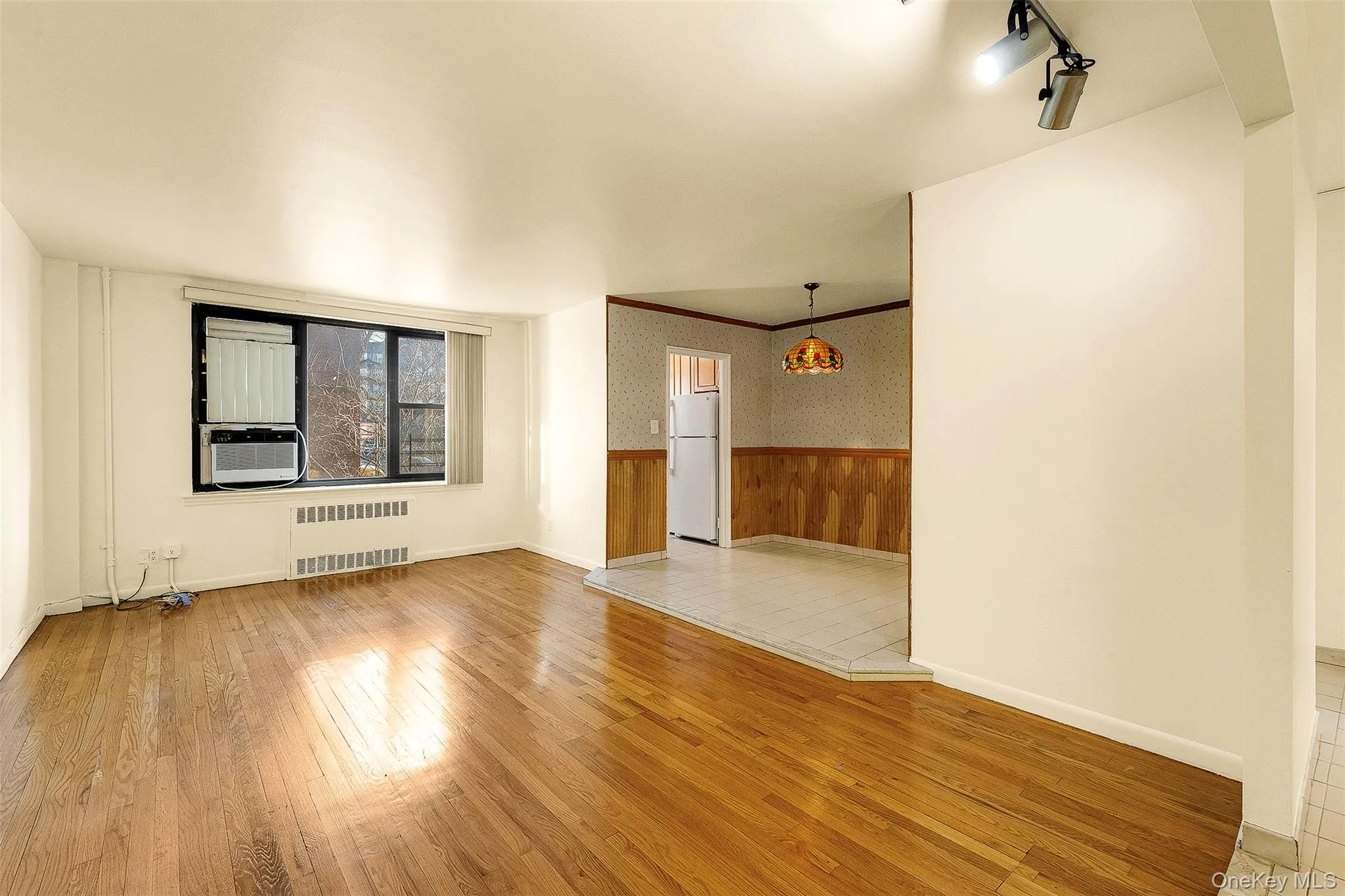 Unfurnished room with wallpapered walls, wainscoting, light wood finished floors, radiator, and track lighting Unfurnished room with wallpapered walls, wainscoting, light wood finished floors, radiator, and track lighting