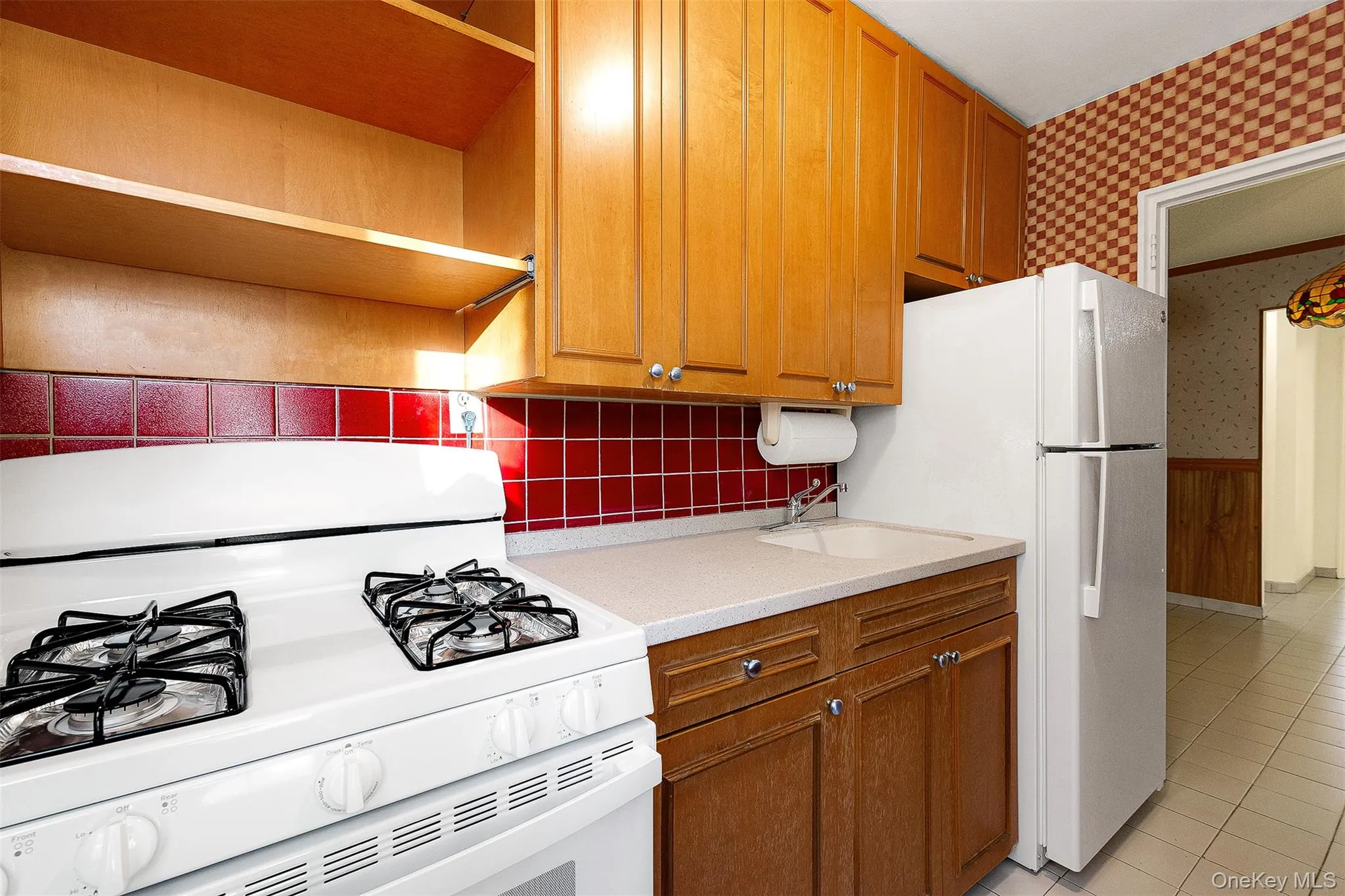 Kitchen featuring wallpapered walls, white appliances, wainscoting, brown cabinets, and light stone counters Kitchen featuring wallpapered walls, white appliances, wainscoting, brown cabinets, and light stone counters