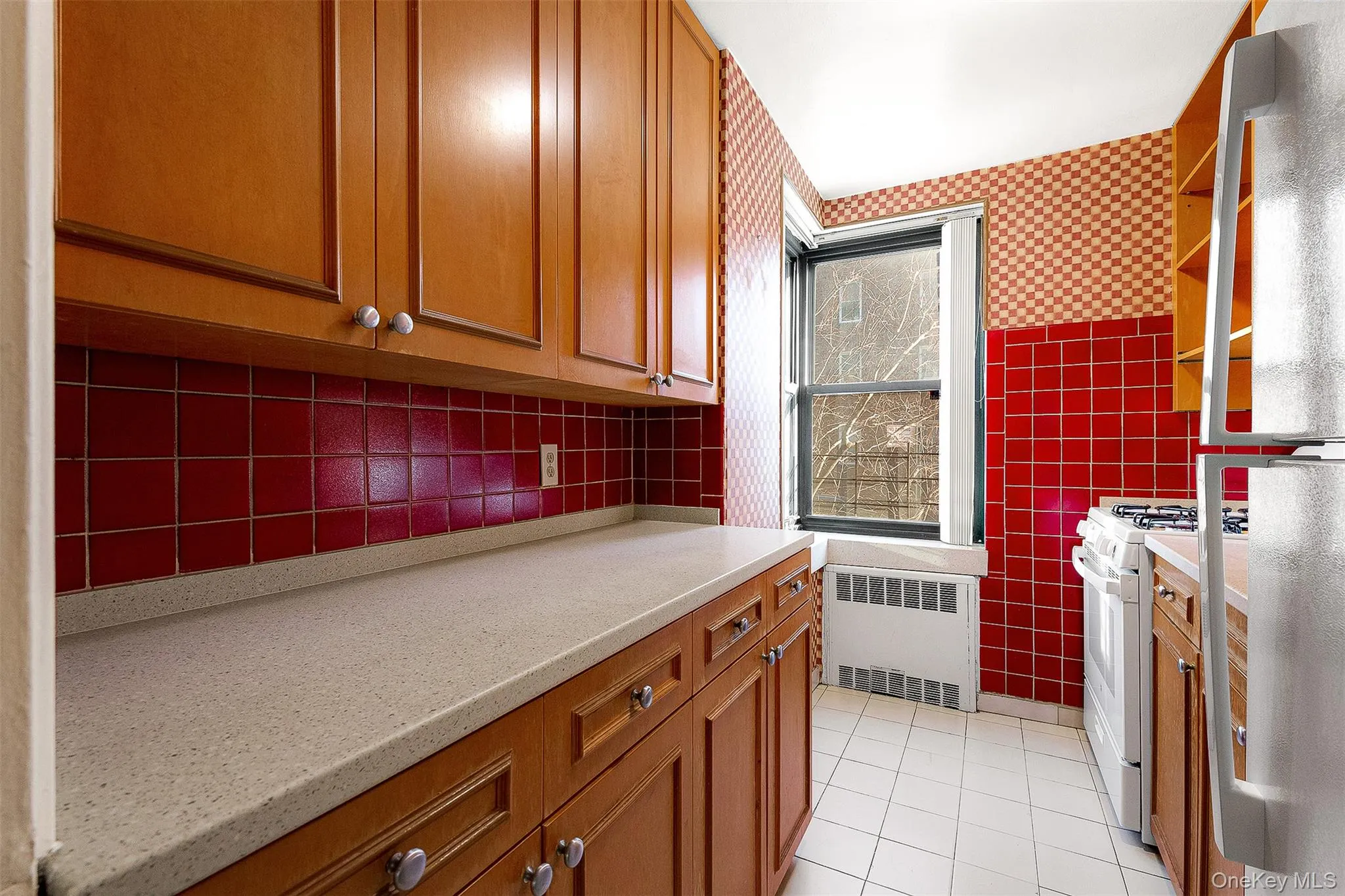 Kitchen with brown cabinetry, freestanding refrigerator, white range with gas stovetop, and radiator Kitchen with brown cabinetry, freestanding refrigerator, white range with gas stovetop, and radiator